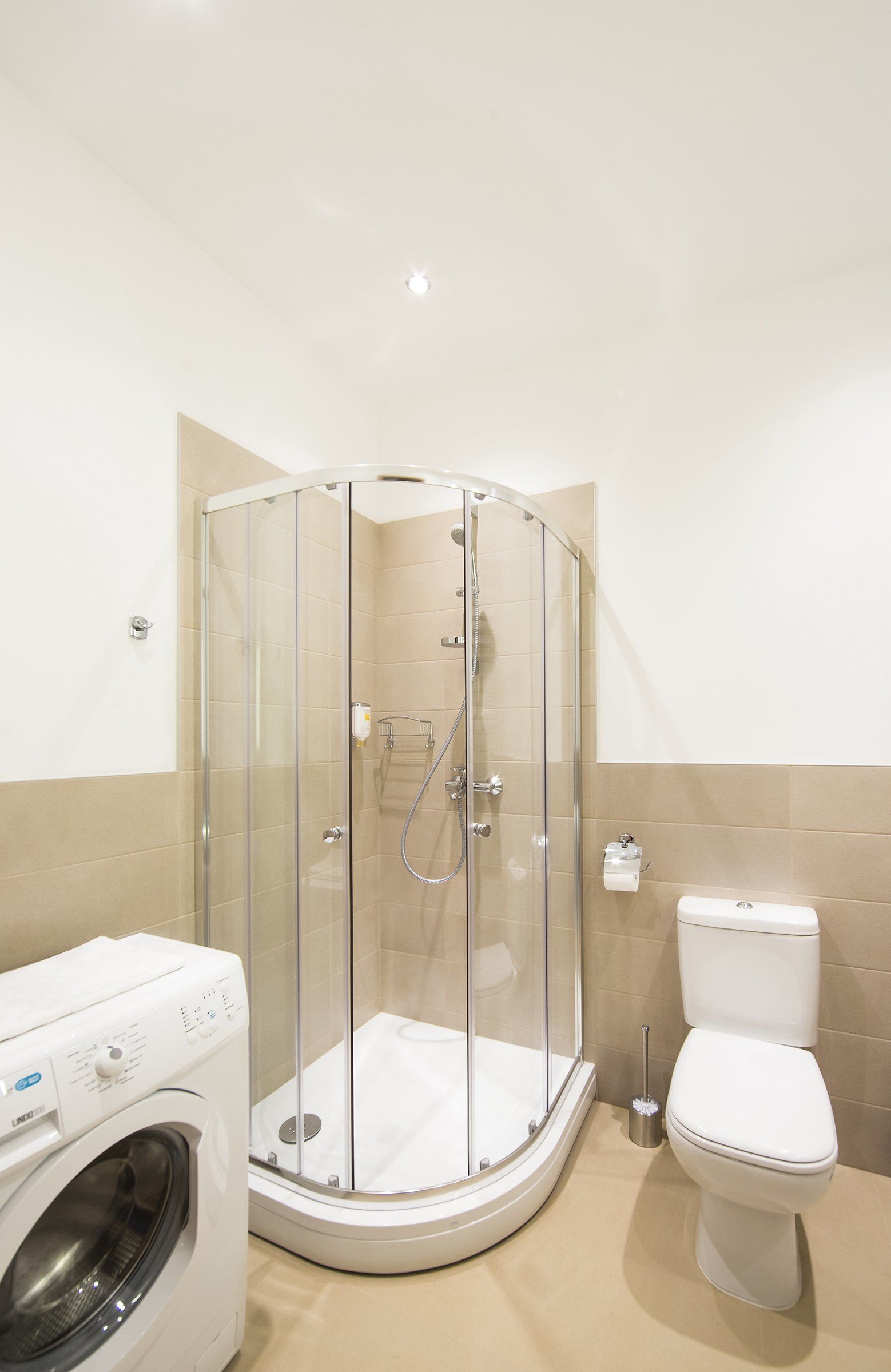 A bathroom with a washing machine , toilet and shower stall.