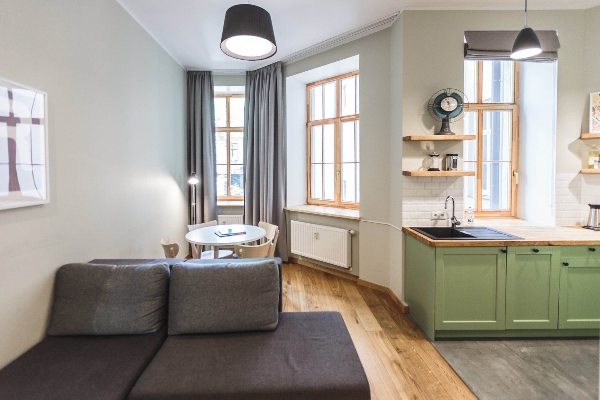 A living room with a couch and a kitchen with green cabinets.