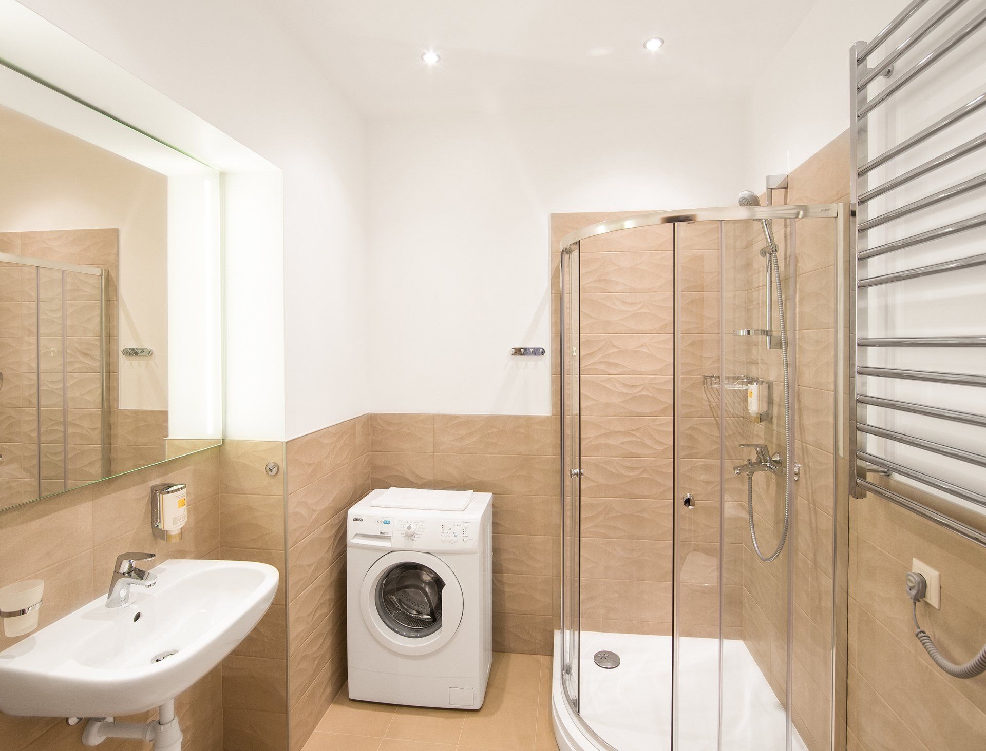 A bathroom with a washing machine , sink and shower.
