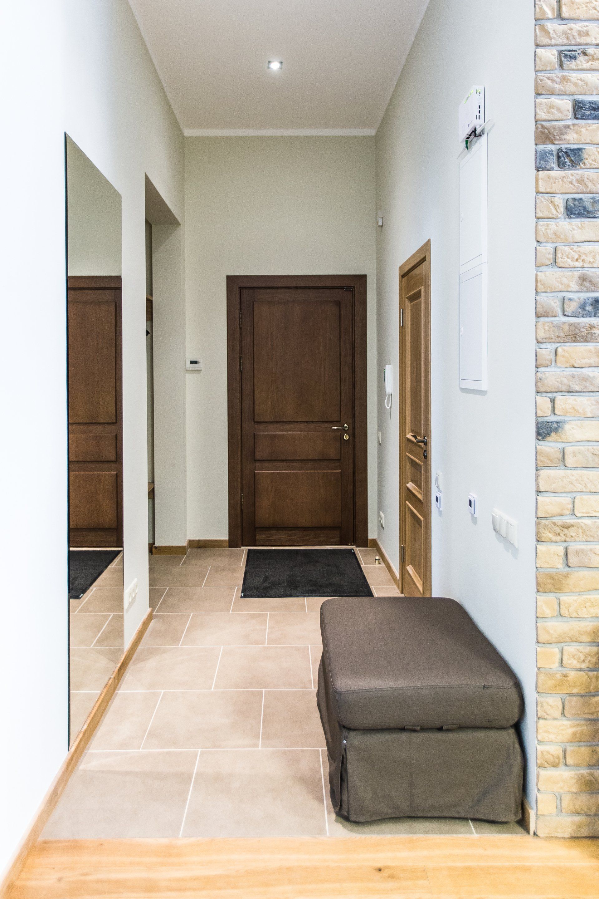 A hallway with a bench , mirror , and brick wall.