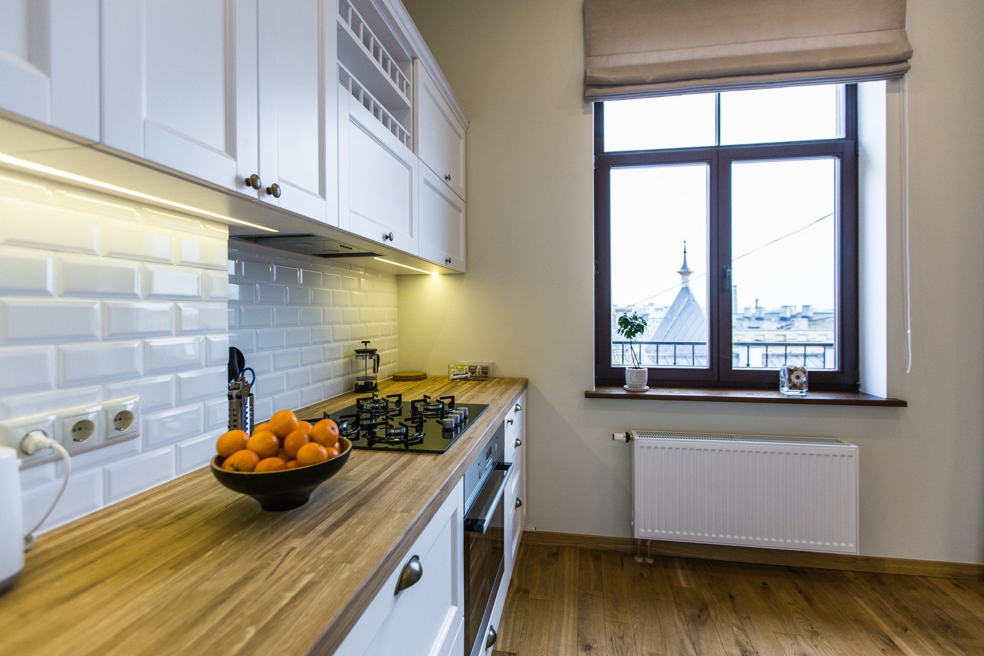 A kitchen with a bowl of oranges on the counter and a window.