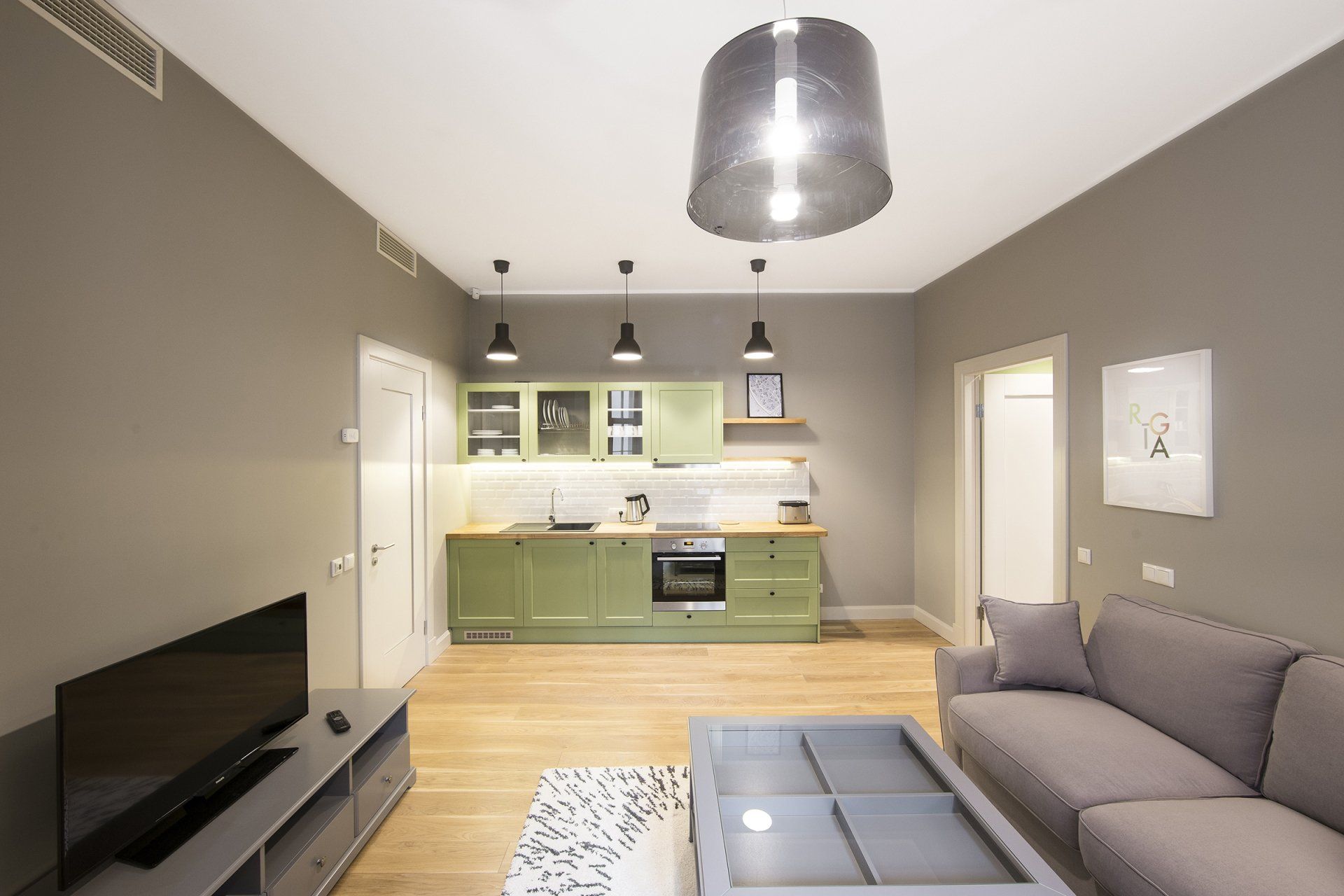 A living room with a couch , television , coffee table and kitchen.