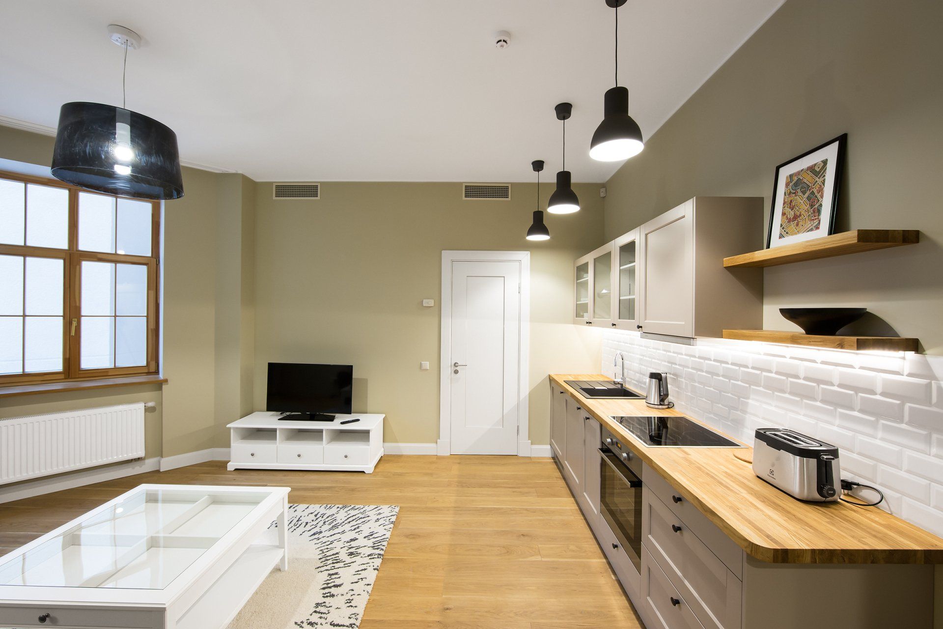 A living room with a kitchen and a flat screen tv.