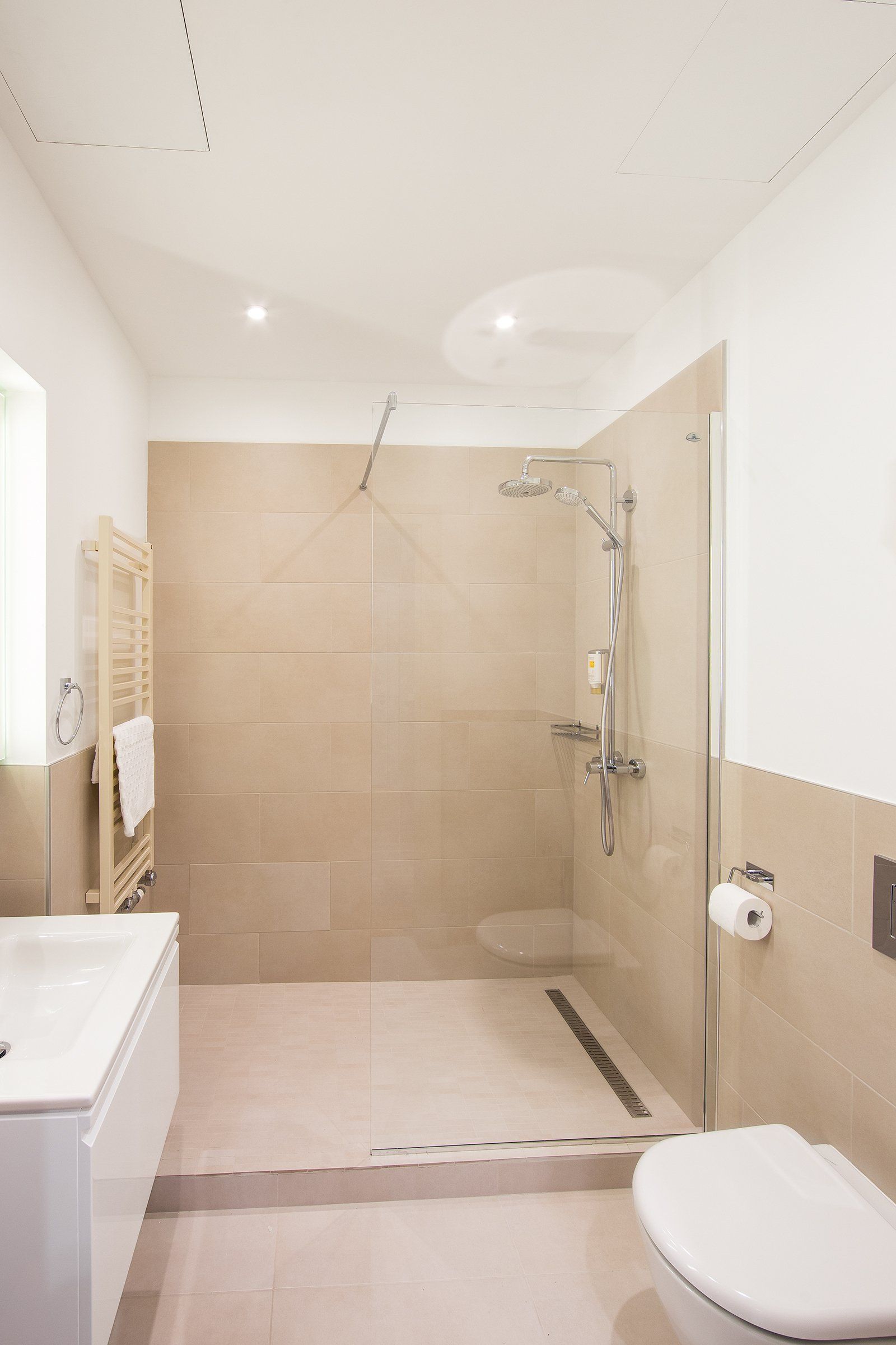 A bathroom with a walk in shower , toilet , sink and towel rack.