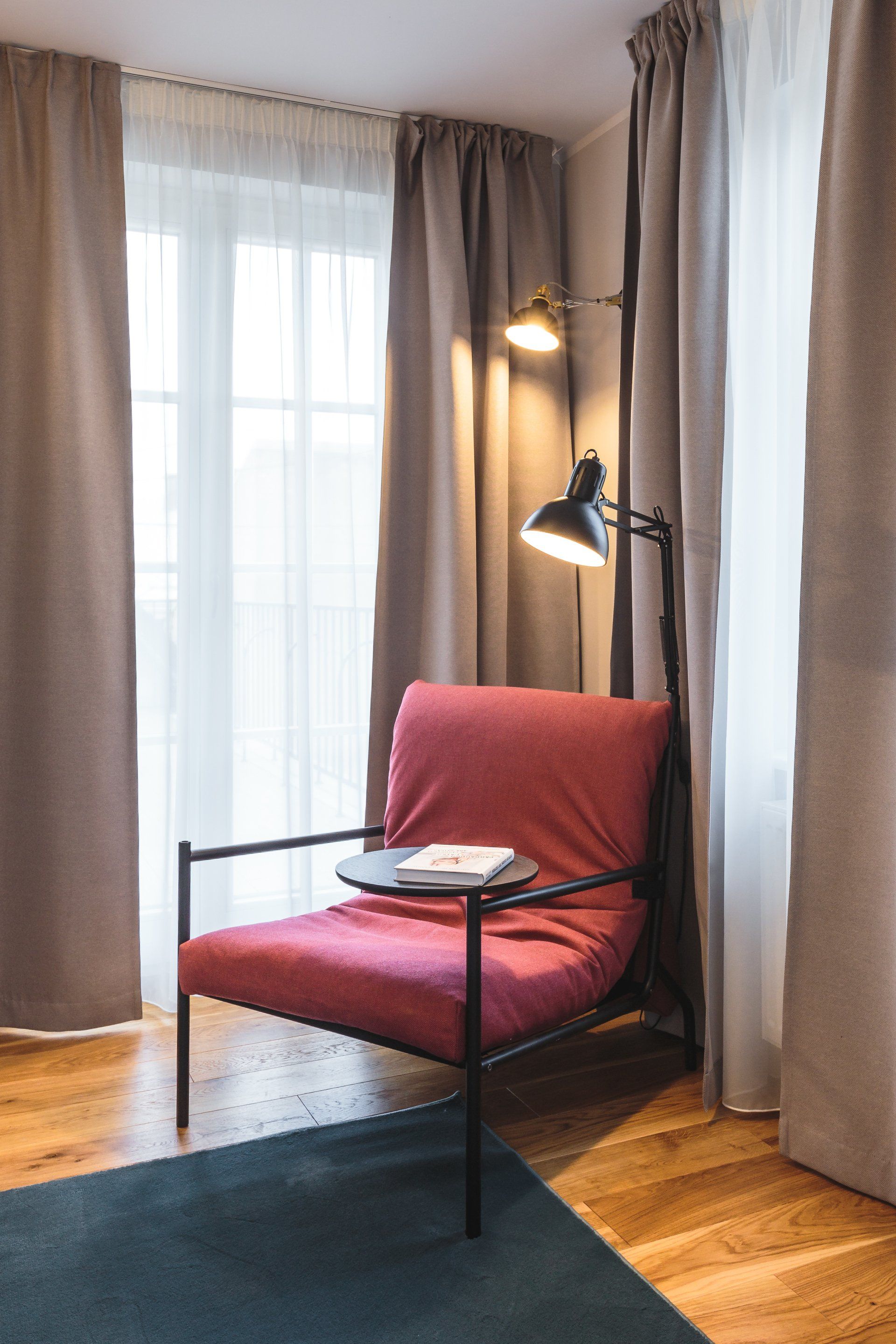 A red chair is sitting in a room next to a window.