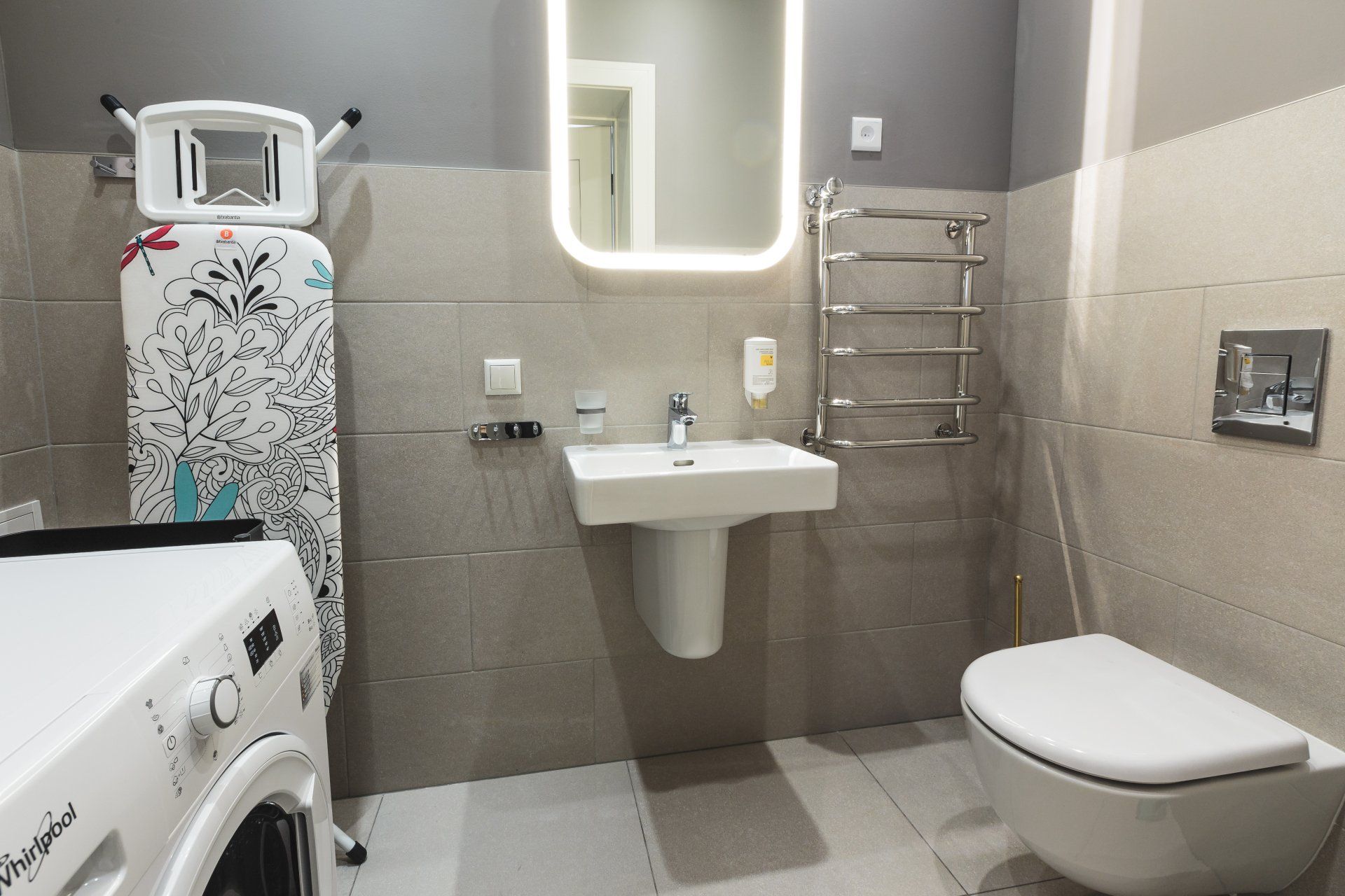 A bathroom with a washing machine , toilet , sink and mirror.