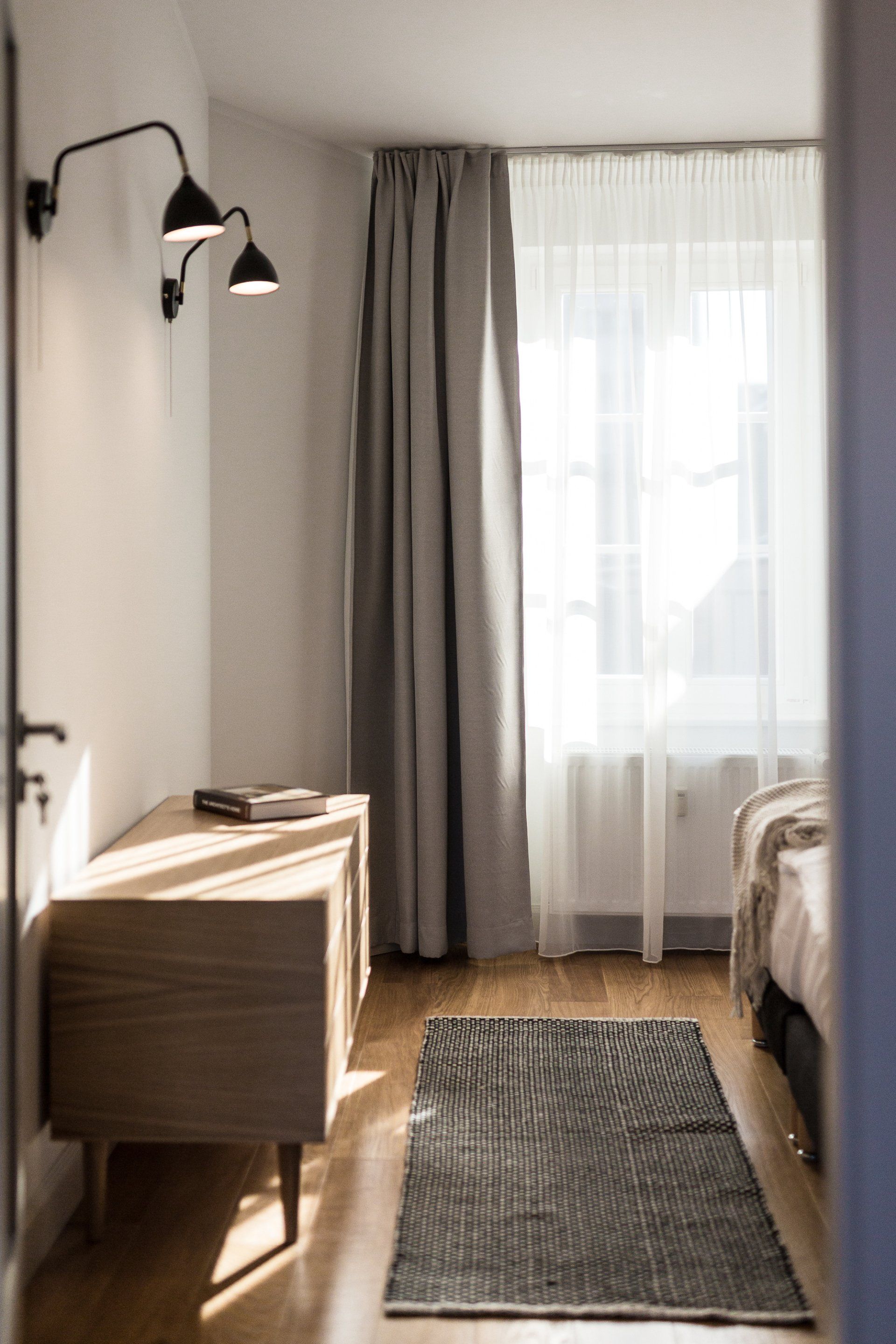 A bedroom with a bed , dresser , rug and window.
