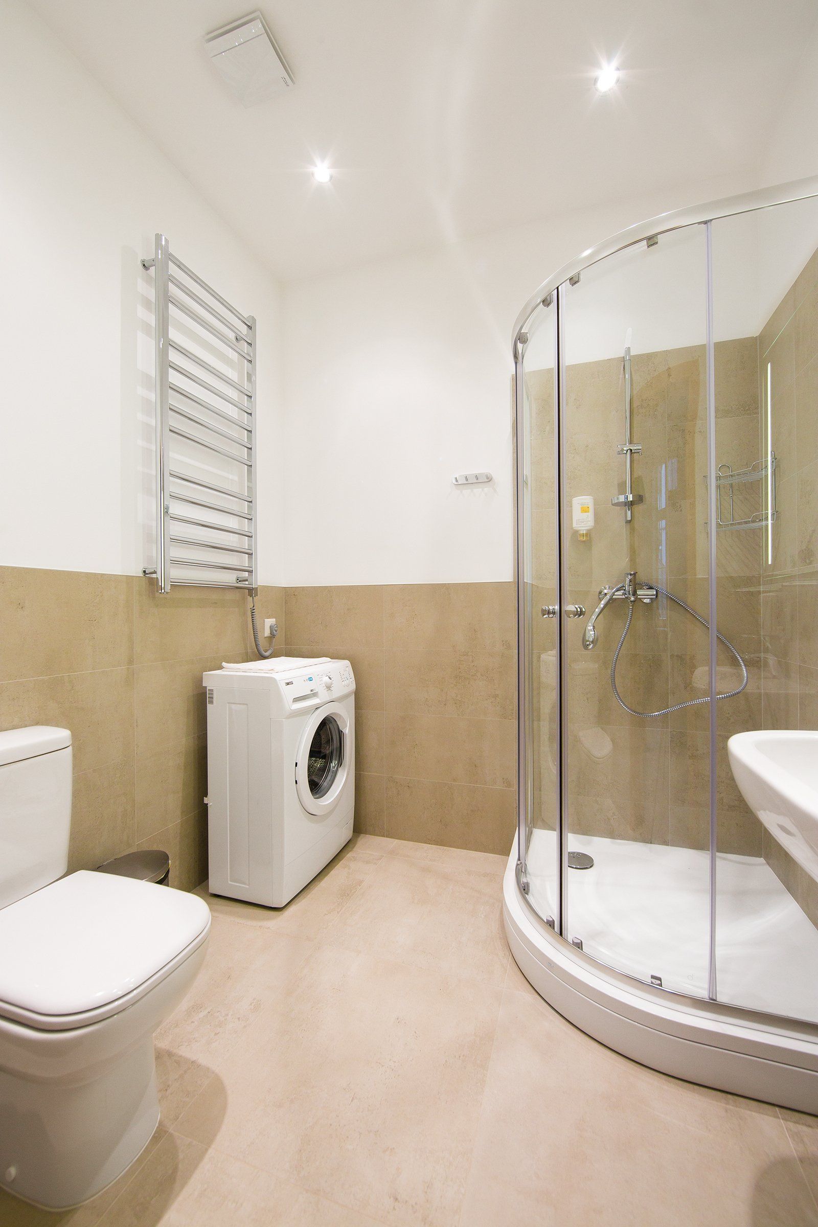 A bathroom with a toilet , sink , washing machine and shower stall.
