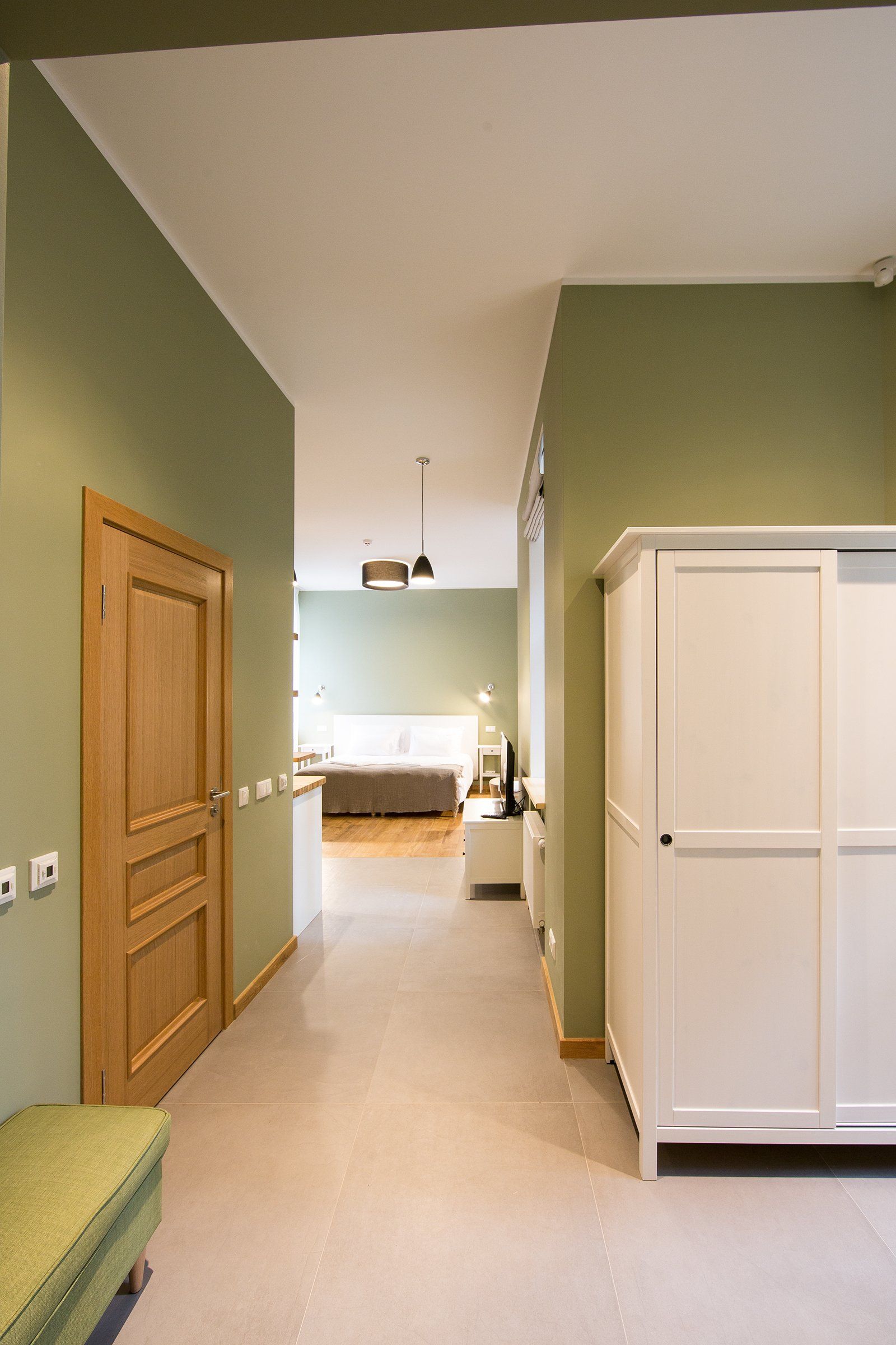 A hallway leading to a bedroom with green walls and a white wardrobe.
