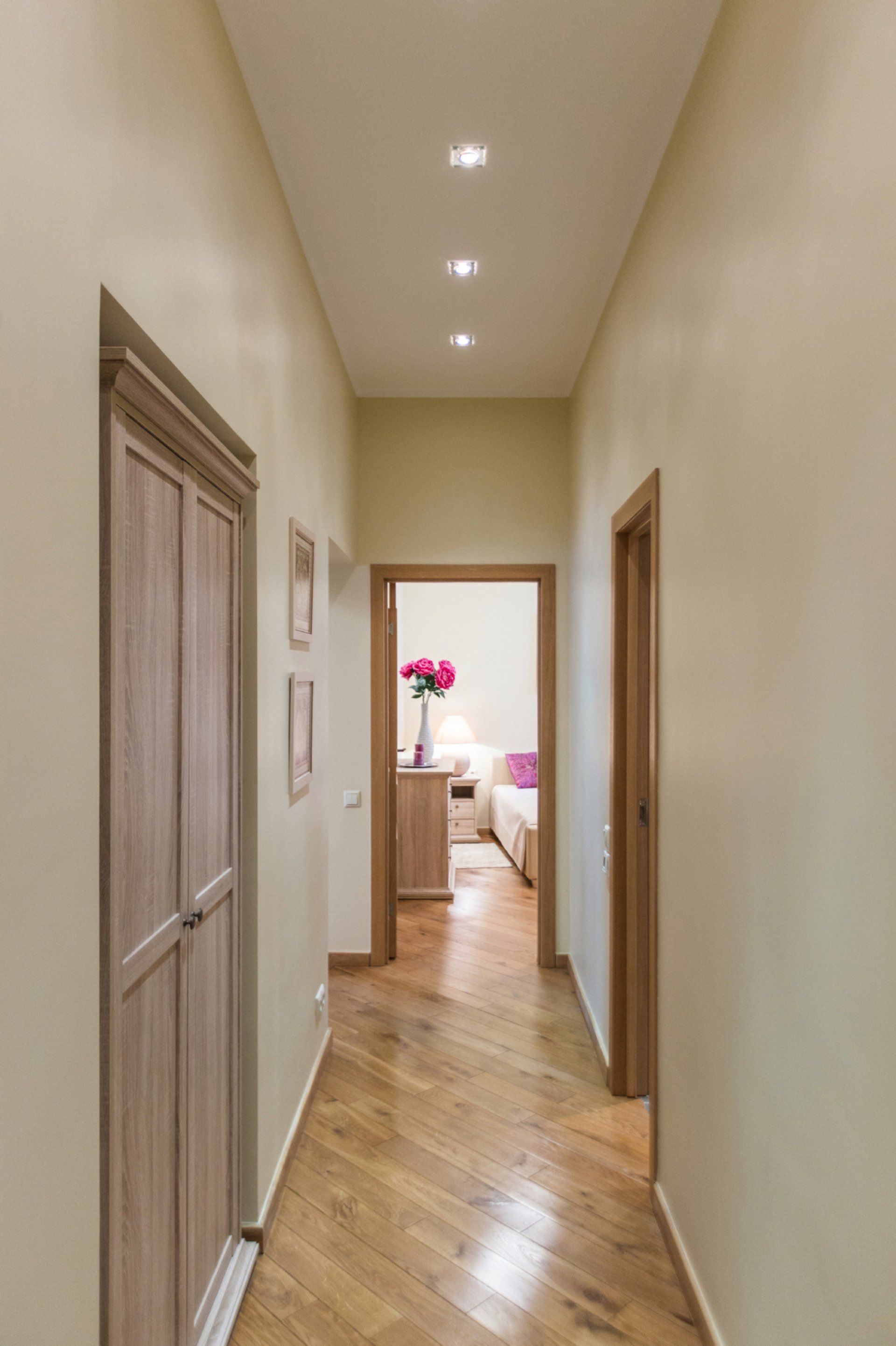 A long hallway with wooden floors and doors leading to a bedroom.