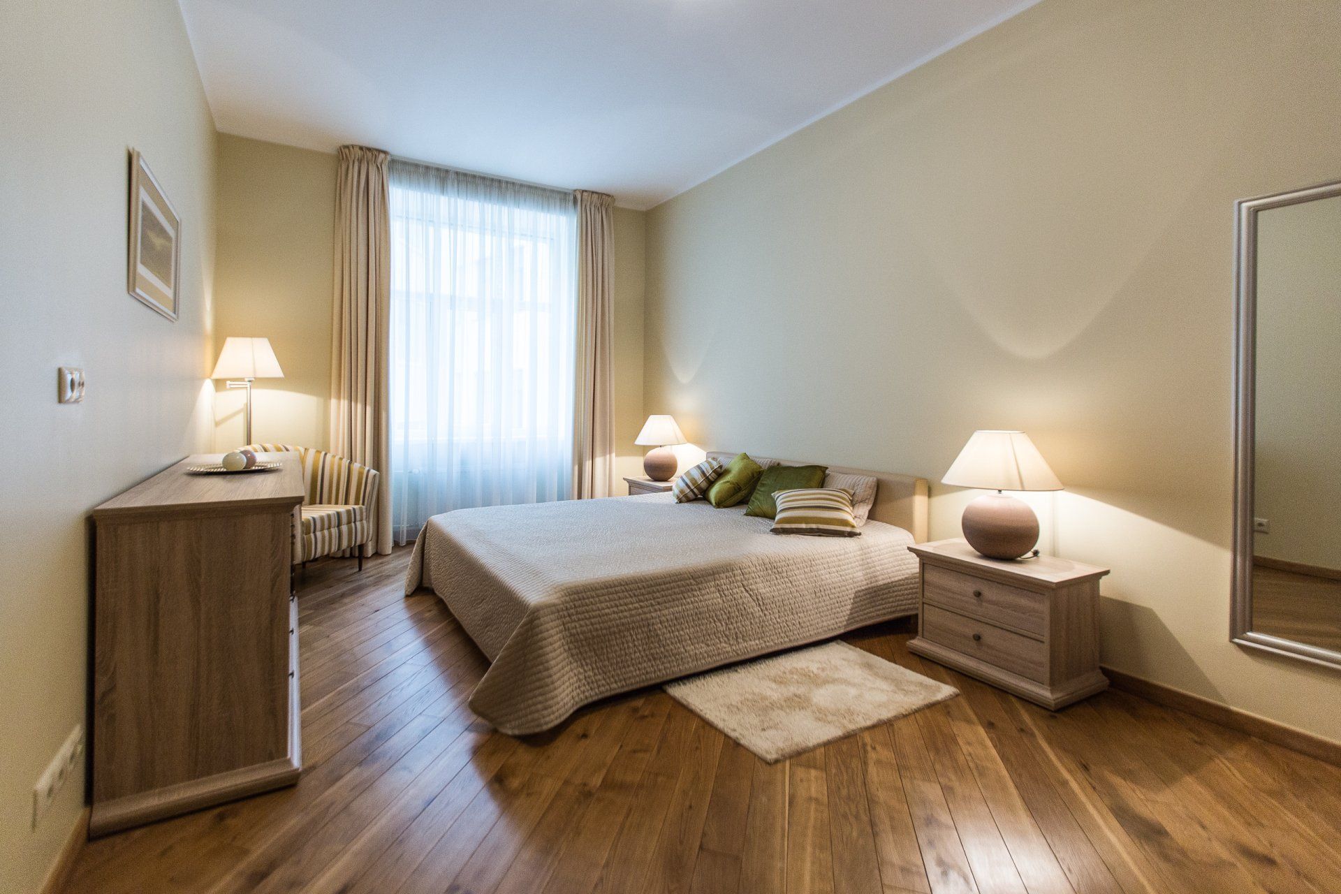A bedroom with a large bed , nightstands , lamps and a mirror.