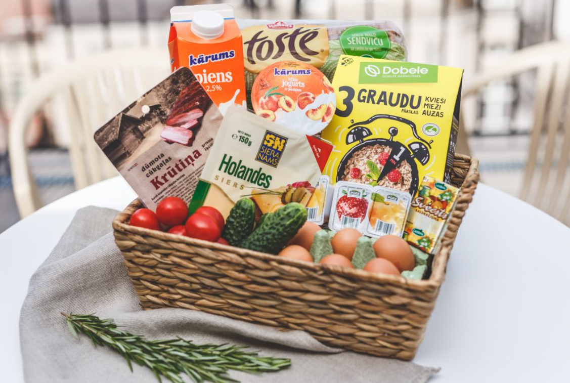 A wicker basket filled with eggs , tomatoes , cucumbers and other food items on a table.