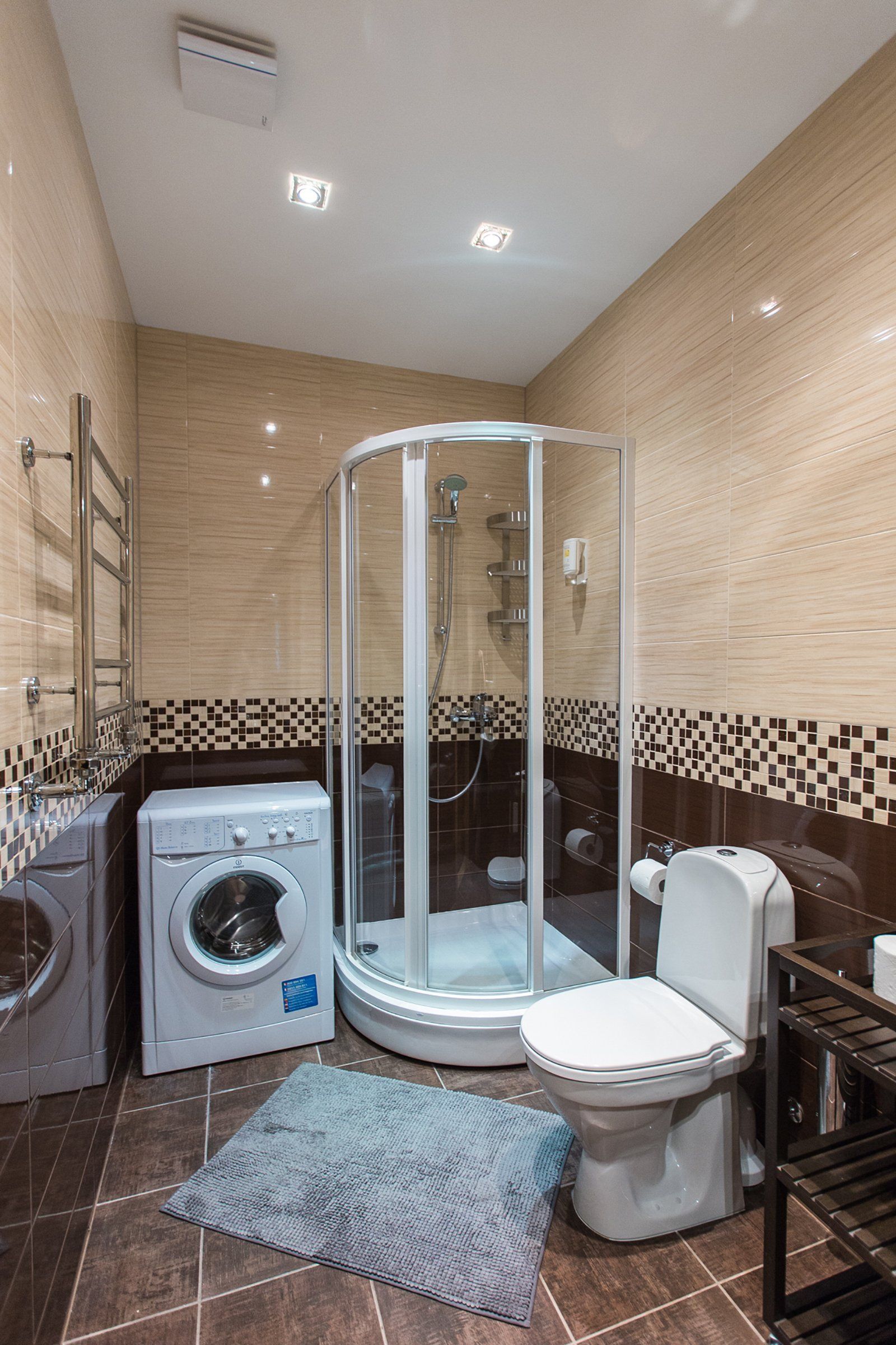 A bathroom with a toilet , shower , washer and dryer.