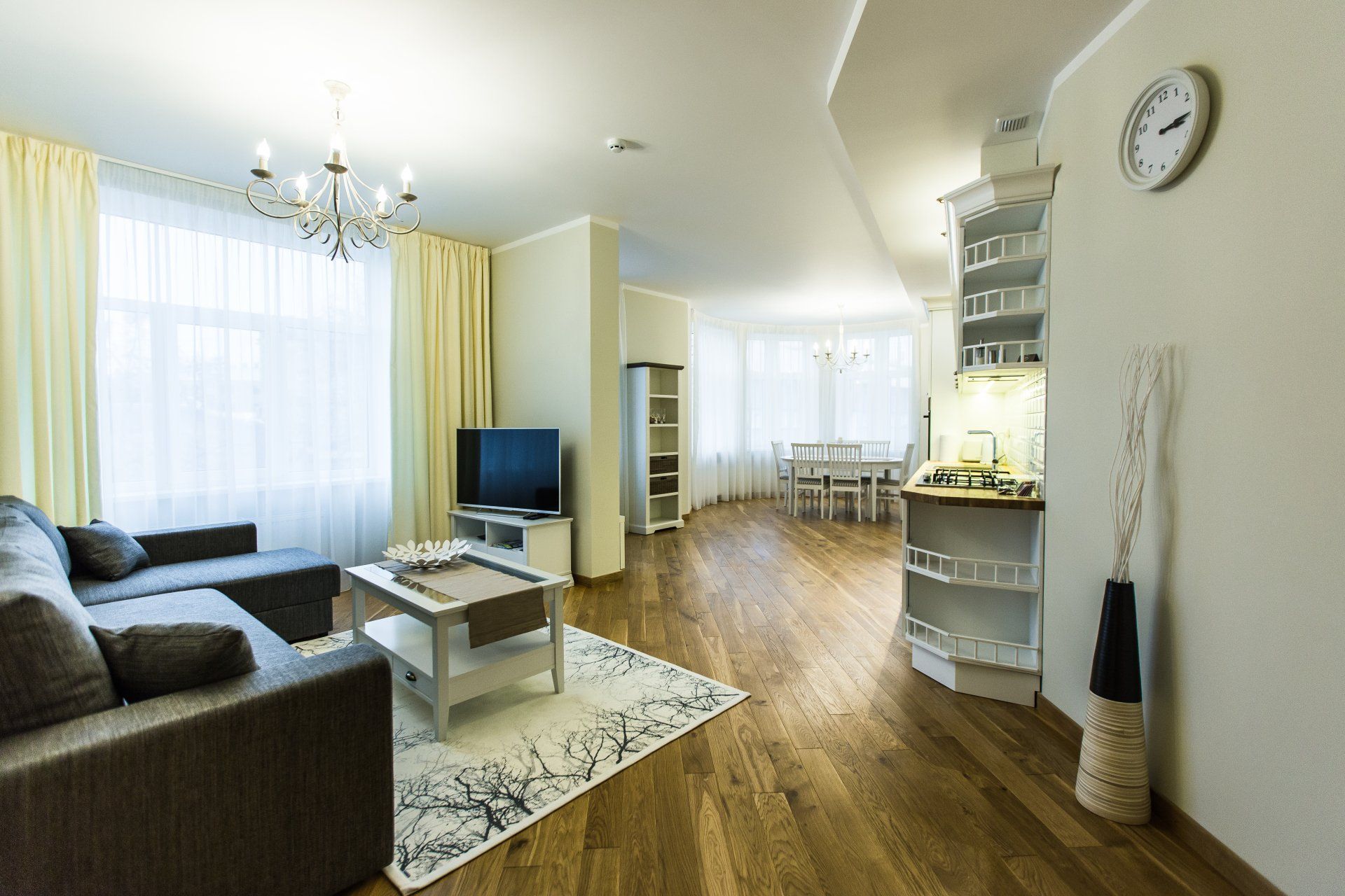 A living room with a couch , table , television and a clock on the wall.
