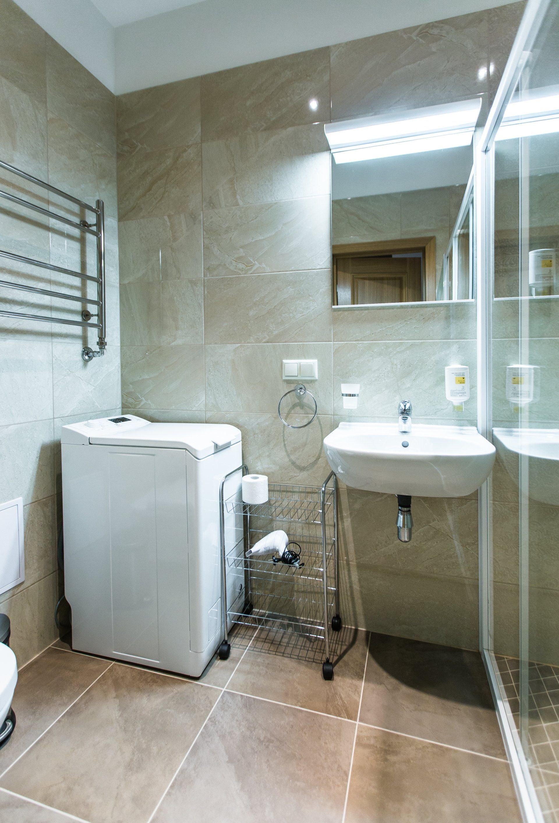 A bathroom with a washing machine , sink , toilet and mirror.