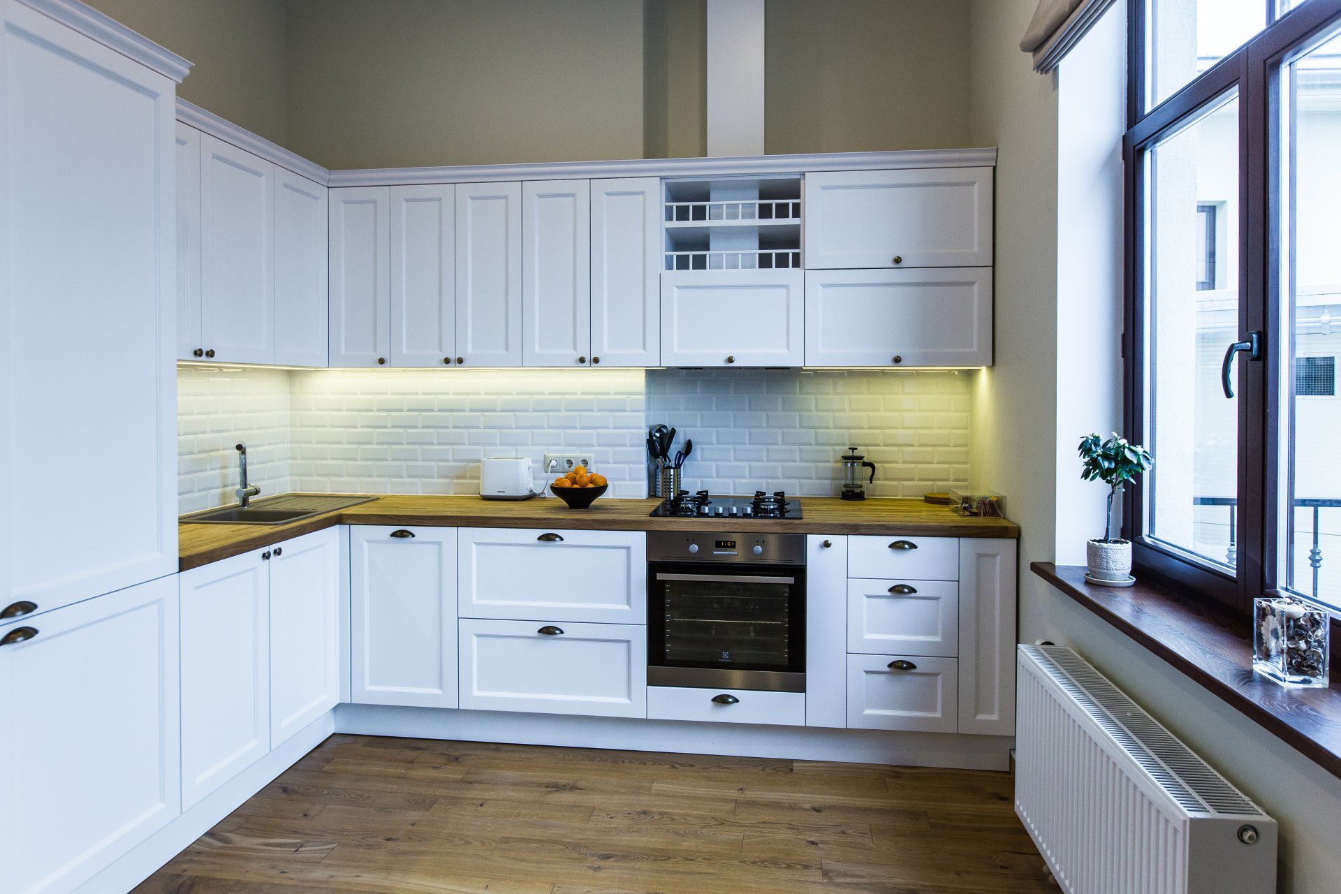 A kitchen with white cabinets , a stove , a sink , and a window.