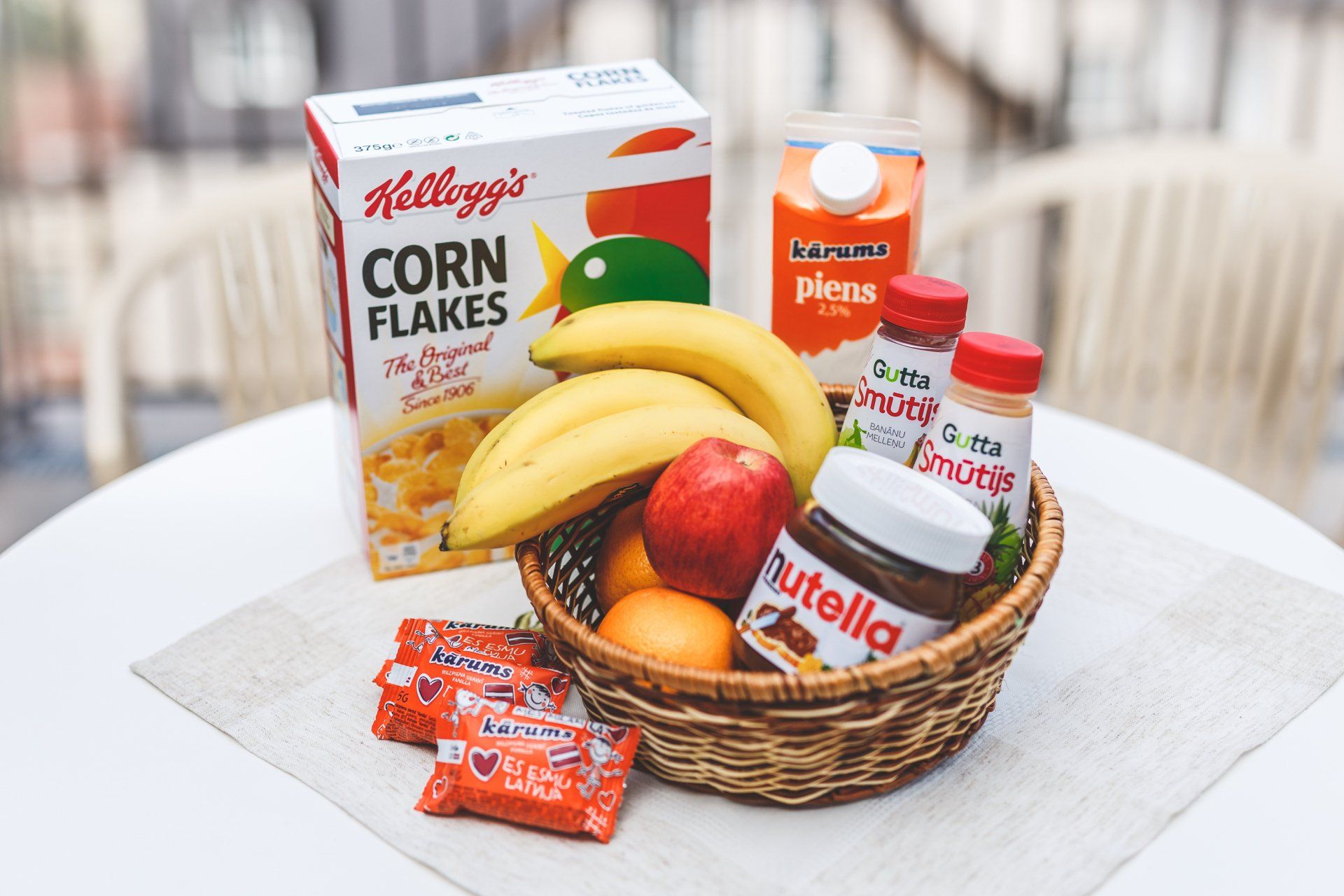 A basket filled with fruit and a box of corn flakes on a table.