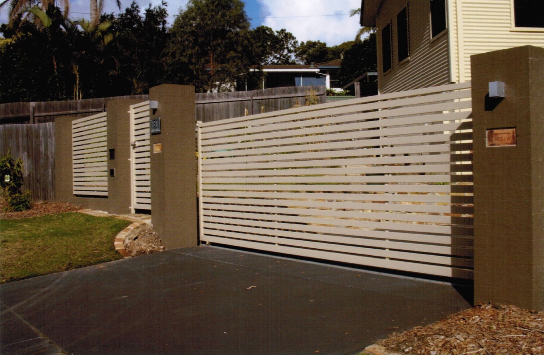 A white fence is surrounding a driveway in front of a house — Fabricator In Coffs Harbour, NSW