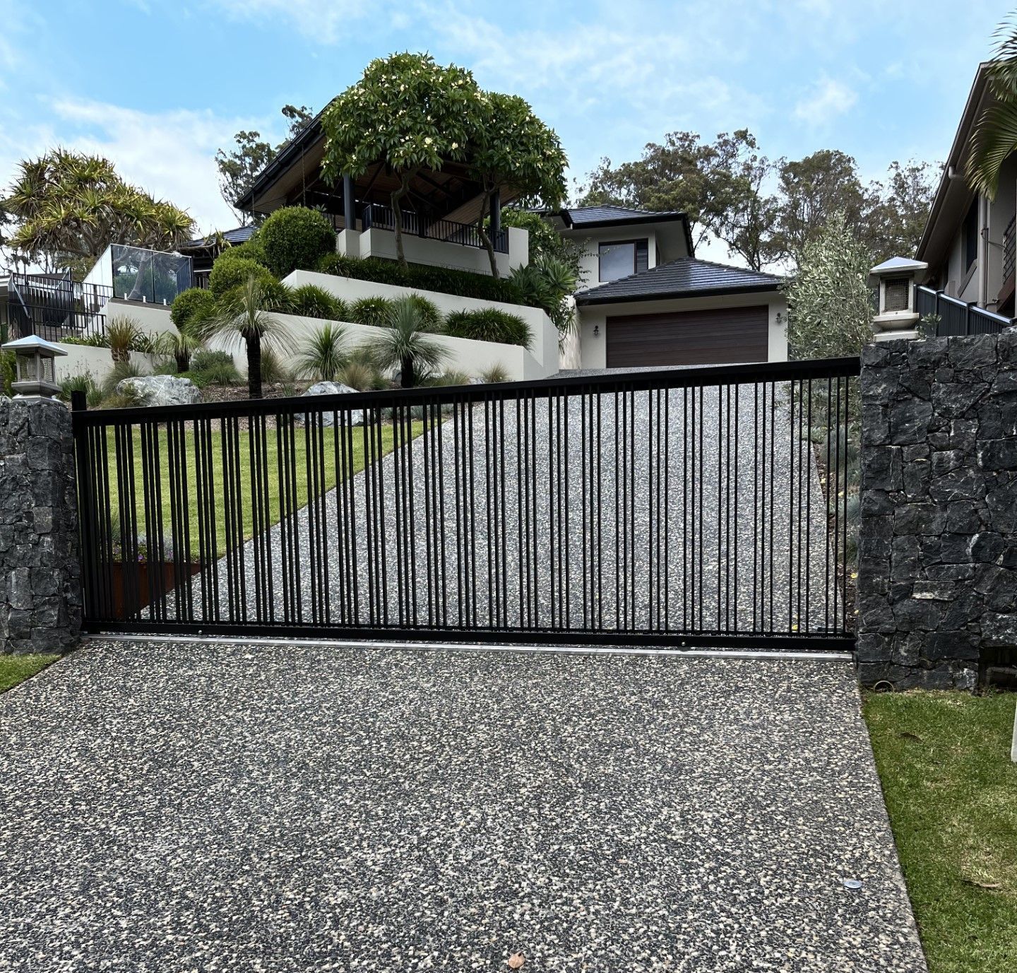 Black sliding driveway gate between stone pillars at a residential property.