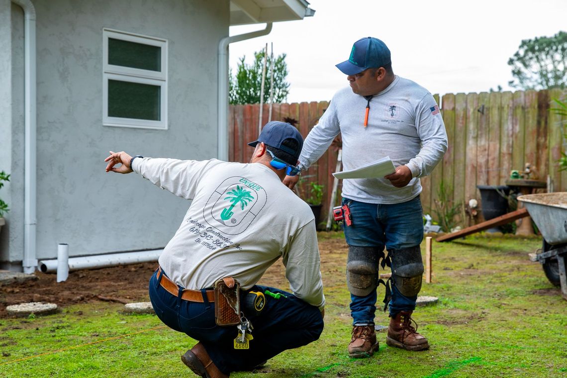 Two construction workers in uniforms discussing plans in a residential yard near a stucco house.