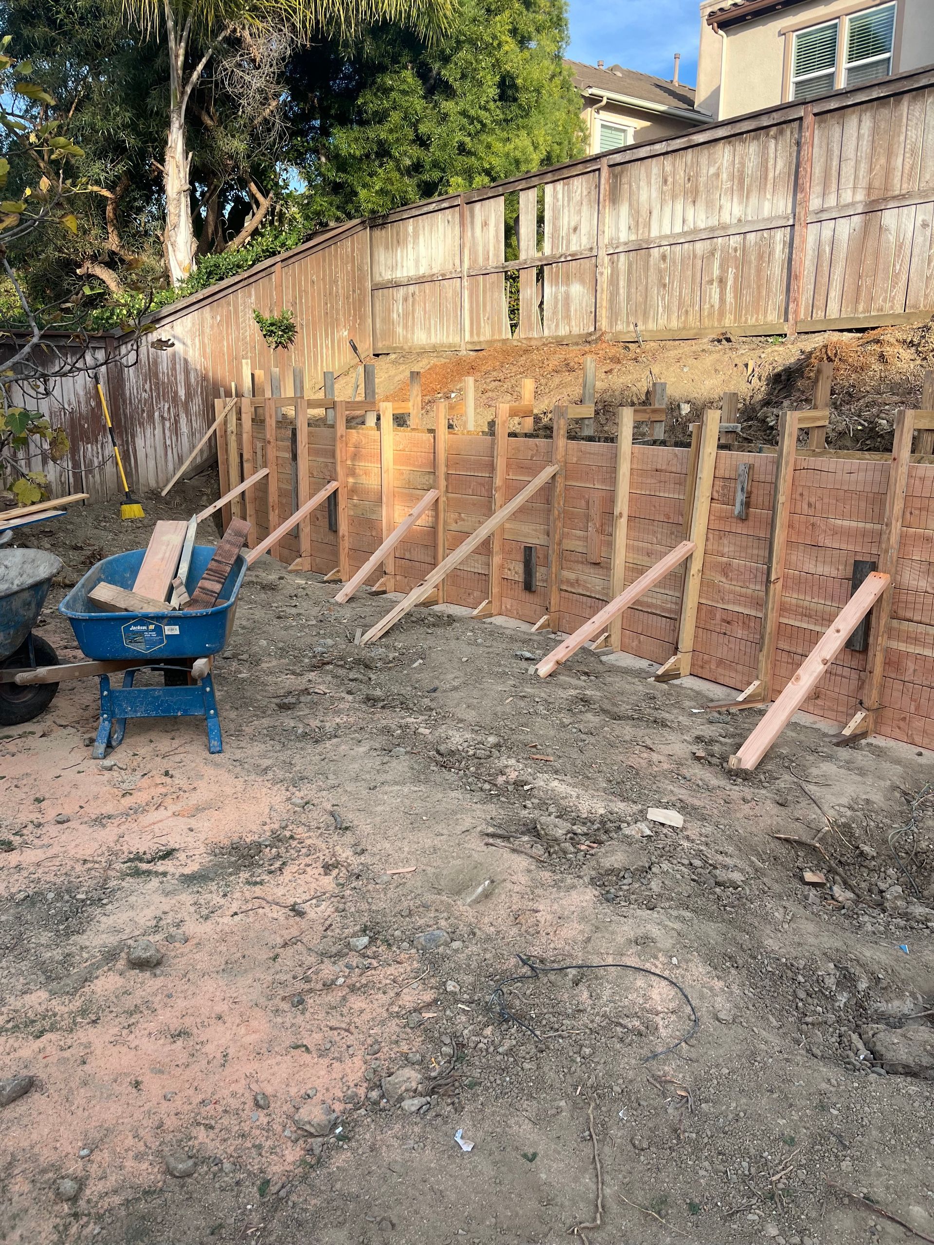 A retaining wall under construction with wooden forms and diagonal support braces in a backyard.