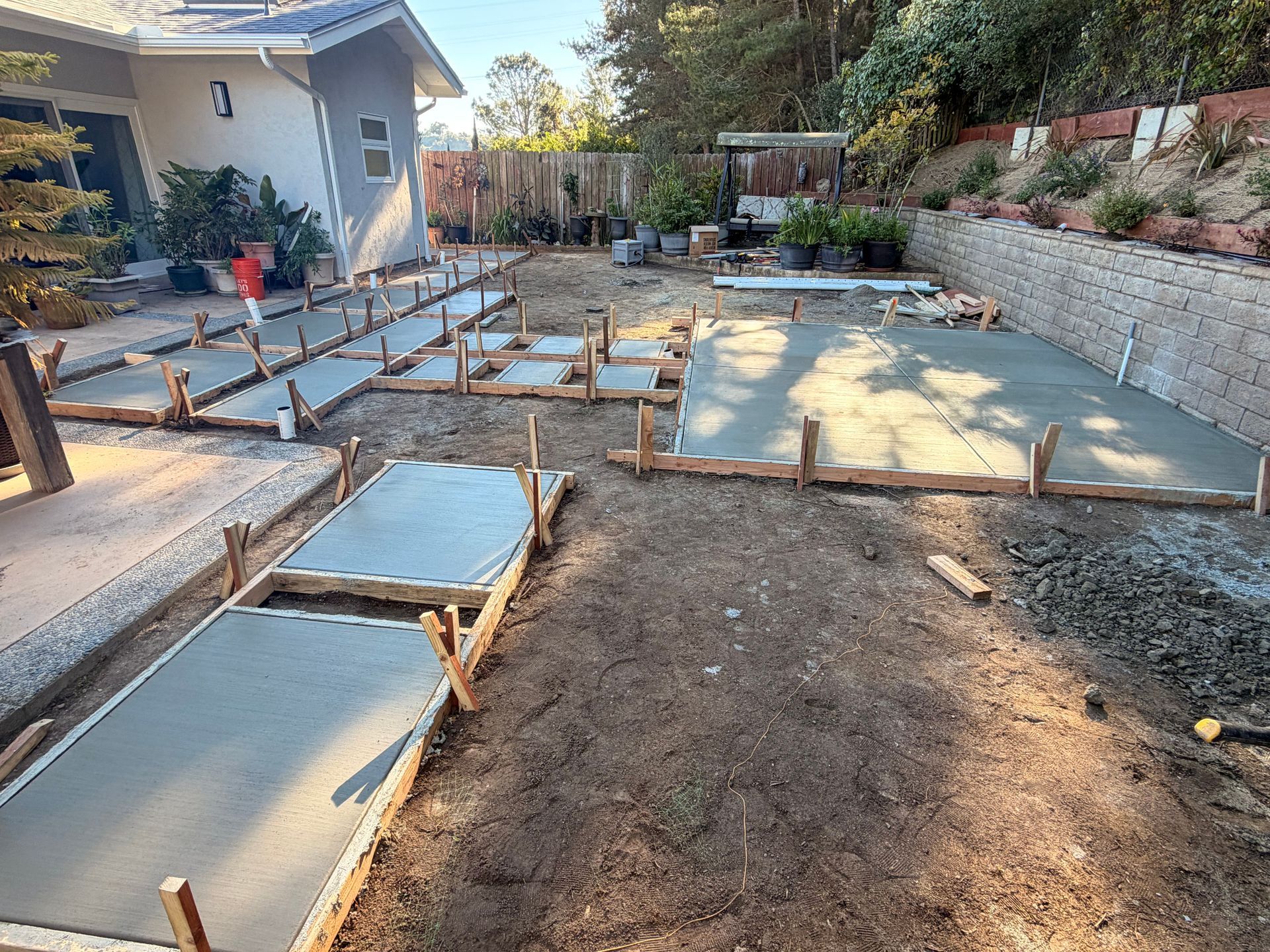Freshly poured concrete patio sections and paths under construction in a residential backyard.