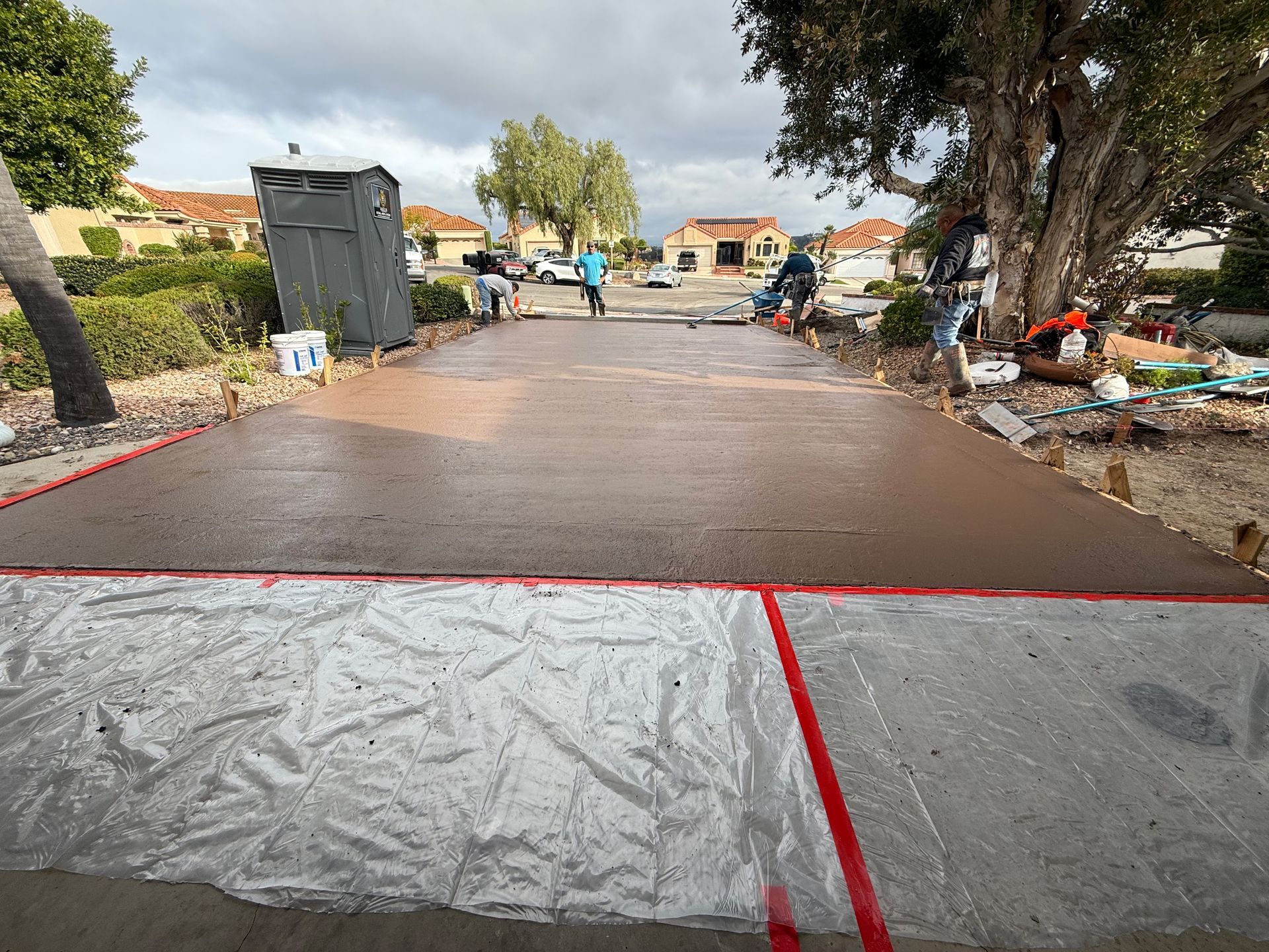 A freshly poured concrete driveway in a residential neighborhood with workers in the background.