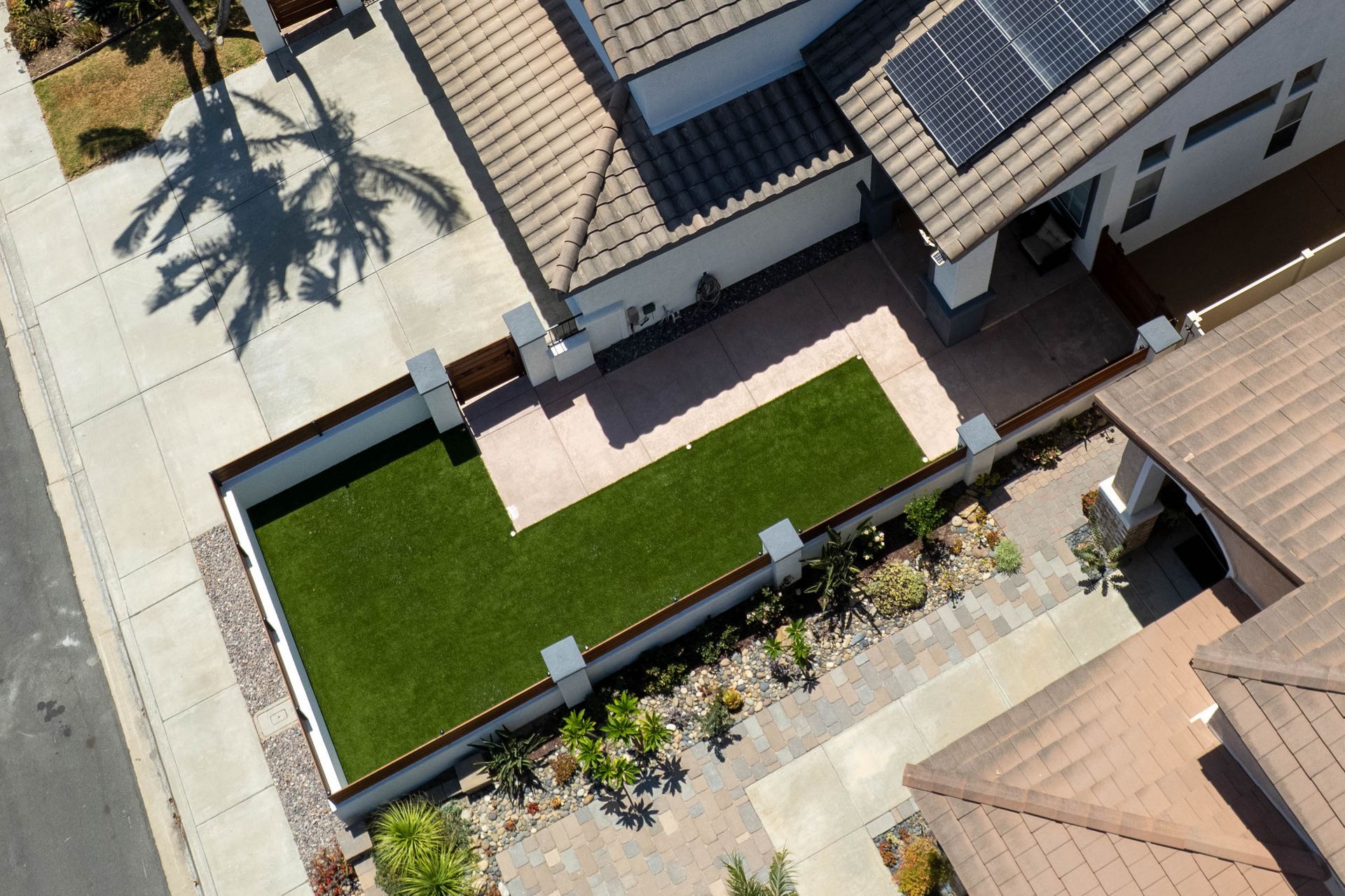 A blue patterned outdoor rug sits next to a front yard landscaped with brown gravel, small green shrubs, and succulents.