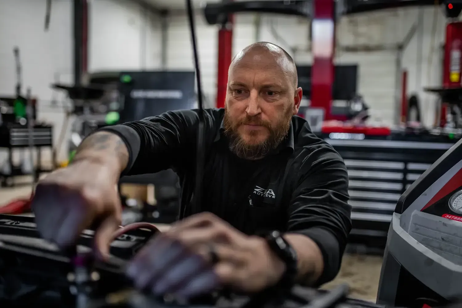 Technician operating a red-and-black machine with gauges and hoses in a workshop.