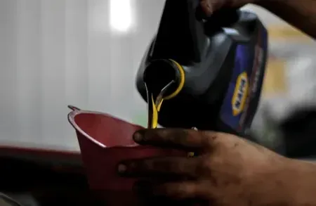 Hands pouring liquid from a black bottle into a red bowl on a table