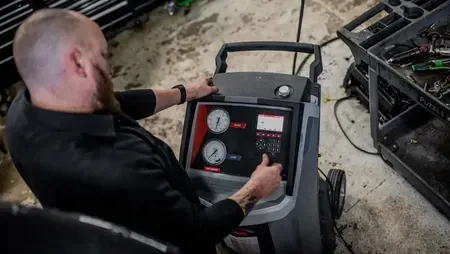 Technician adjusting controls on a welding machine in a workshop, with tools and cables nearby.