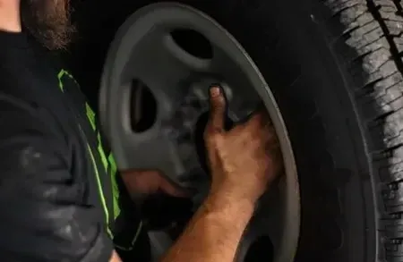 Mechanic tightening a car wheel on a dark vehicle with a wrench