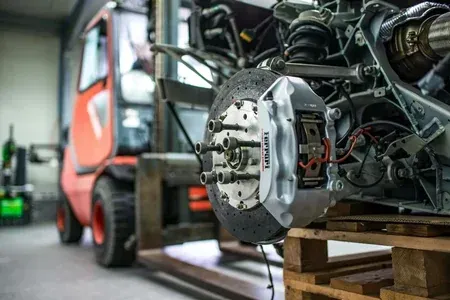 Forklift carrying a heavy vehicle axle and brake assembly on a pallet in a workshop