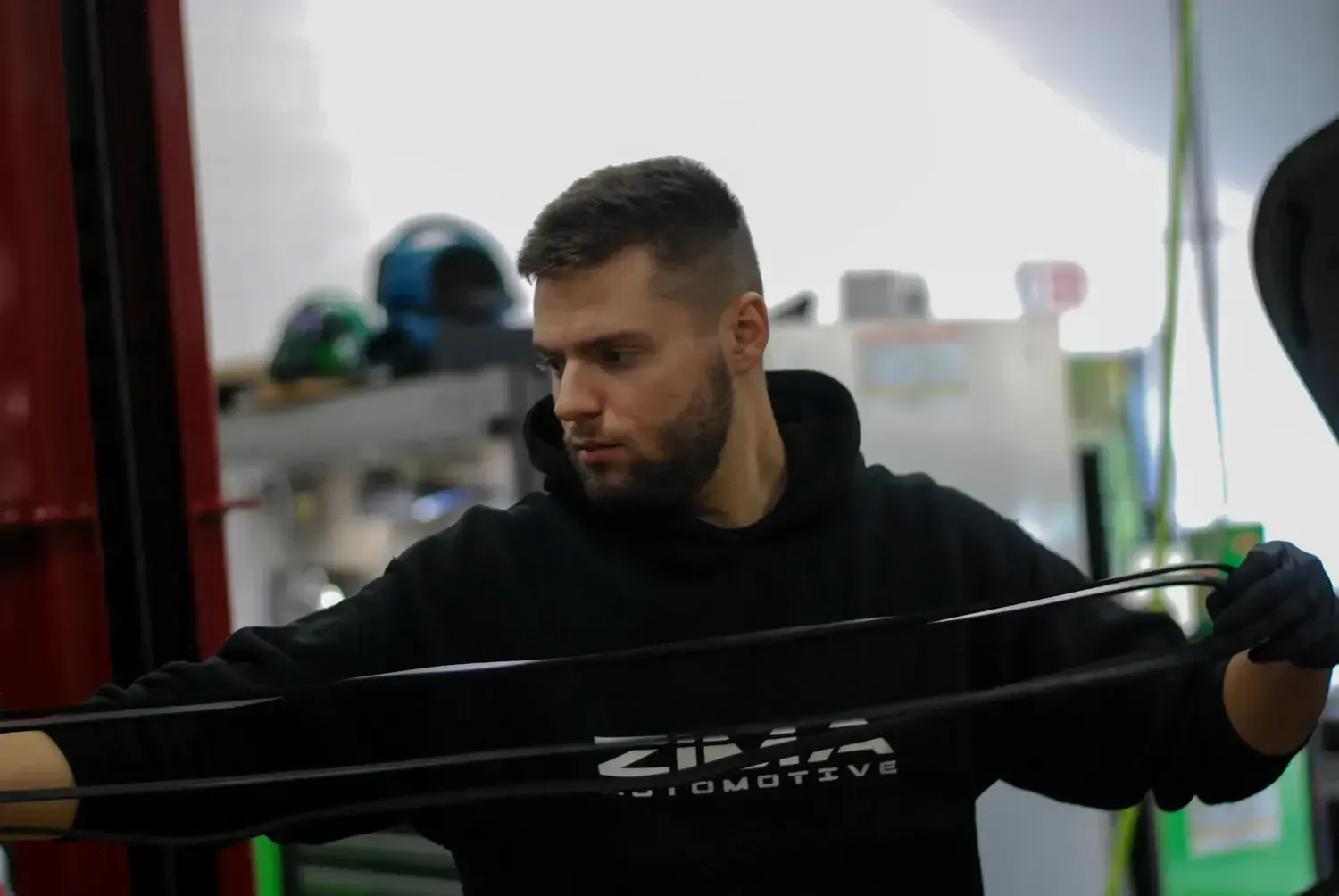 Man stretching a resistance band in a gym, wearing a black hoodie and looking down.