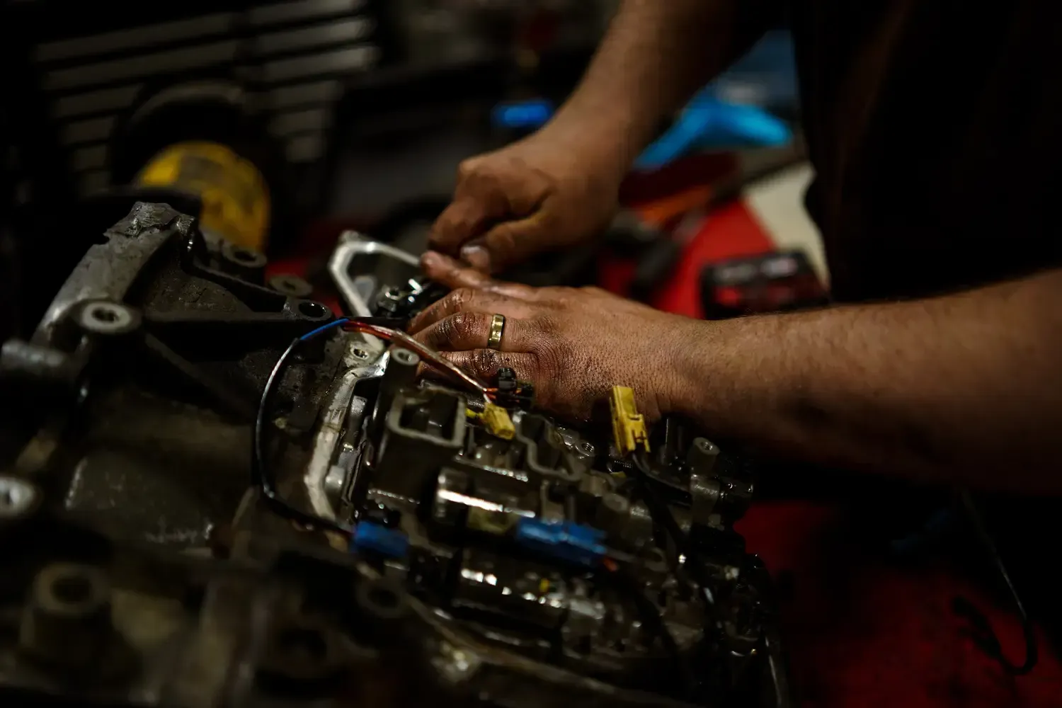Zima mechanic using a power tool to work on a car’s exposed engine in a dark garage