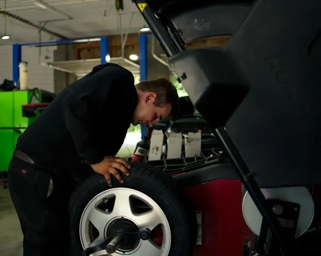 Person tightening a car wheel lug nut with a wrench, close-up in a dim garage
