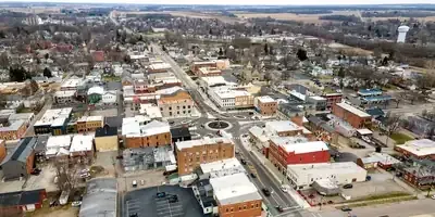 Aerial view of a small town with streets, buildings, and scattered trees under a cloudy sky