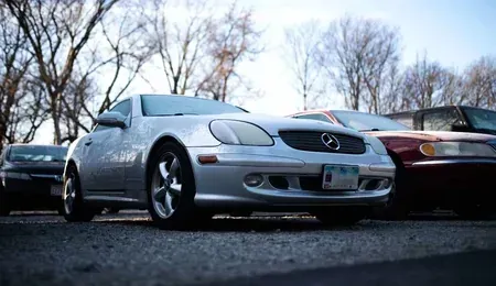 Silver Mercedes sports car parked outdoors beside two other cars under bare trees