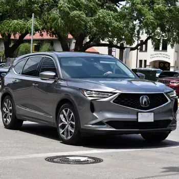 Gray Acura SUV parked on a city street in front of trees and buildings