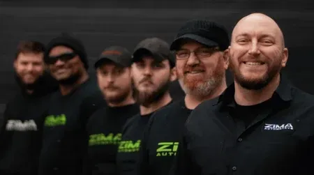 Five men in black shirts and caps stand in a line, smiling against a dark background.