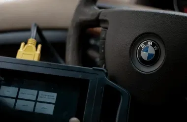 BMW steering wheel with a diagnostic tablet and yellow cable in the foreground