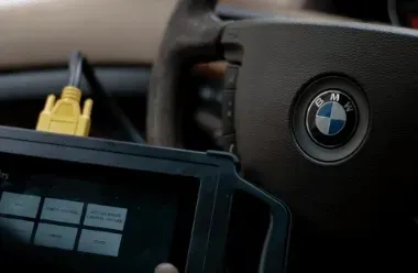 Diagnostic device connected near a BMW steering wheel, showing a screen with menu icons.