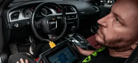 Man sitting in a car interior, using a tablet near the dashboard and steering wheel