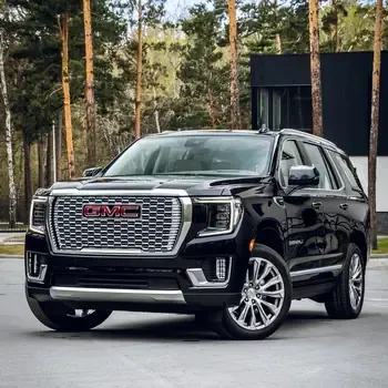 Black GMC SUV parked on pavement in a wooded area, front view with chrome grille and red logo