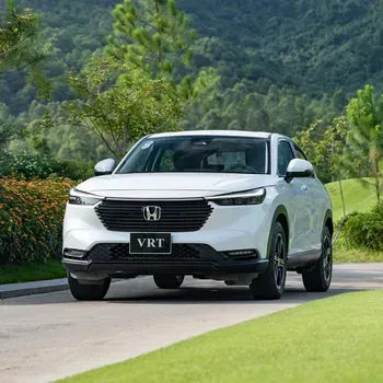 White Honda SUV driving on a paved road beside green lawns and hills under a cloudy sky