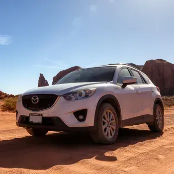 White Mazda SUV parked on a red desert road with sandstone rock formations under a clear blue sky