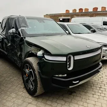Dark green pickup truck with front-end damage and a wrapped side, parked in a lot.