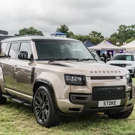 Beige Land Rover Defender SUV parked outdoors at a car show with tents in the background