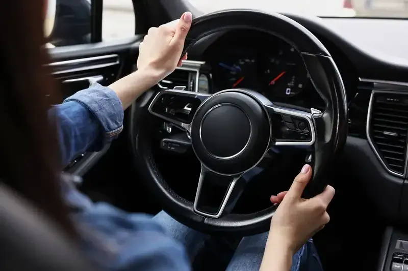 Hands gripping a black steering wheel inside a car interior