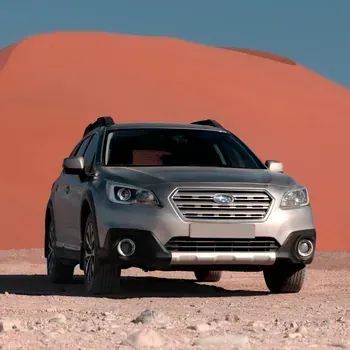 Silver SUV parked on desert sand in front of a large orange dune under a blue sky